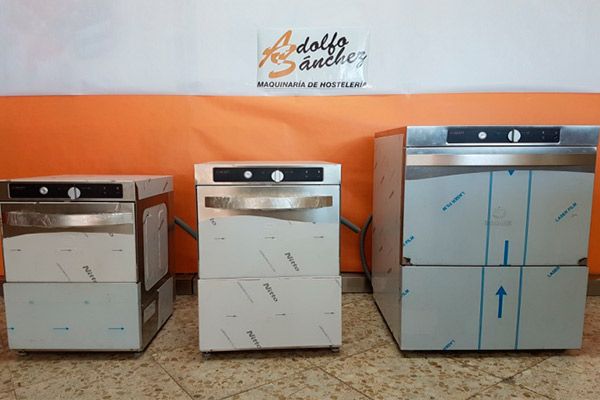 Tres lavavajillas comerciales de acero inoxidable frente a una pared naranja y blanca.