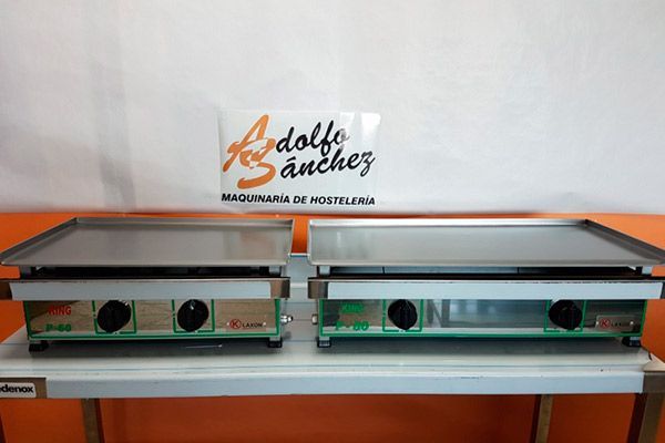 Dos planchas planas sobre una mesa blanca. Son de acero inoxidable con controles verdes y negros. Un logotipo al fondo.