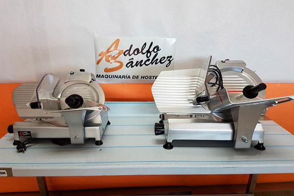 Dos cortadoras de carne plateadas sobre un mostrador blanco con un cartel encima que dice "Rodolfo Sánchez".
