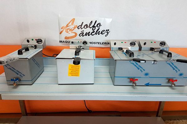 Tres freidoras de acero inoxidable sobre un estante blanco con fondo naranja.