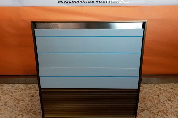 Máquina de hielo comercial de acero inoxidable. Rectangular, con listones horizontales en la base y cinta protectora azul en la parte frontal.