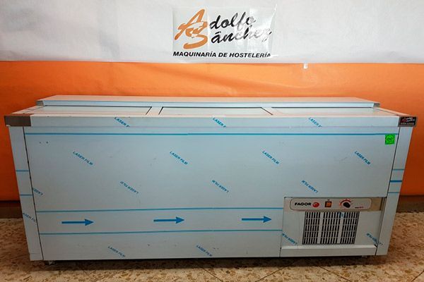 Gran congelador de acero inoxidable con panel de control, frente a una pared naranja y blanca.