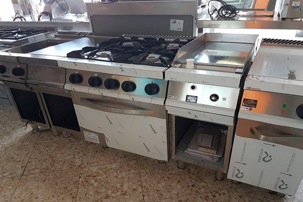 Equipo de cocina comercial de acero inoxidable, que incluye una estufa, una plancha y un horno, en un entorno de cocina.
