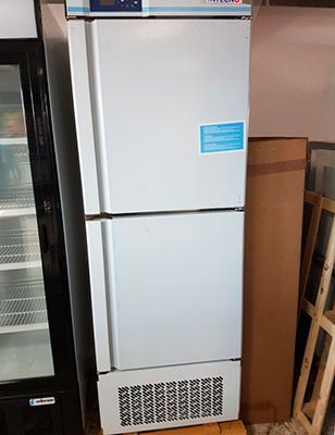 Frigorífico de laboratorio de dos puertas de color blanco con display digital y ventilación en la parte inferior, colocado sobre palet de madera.