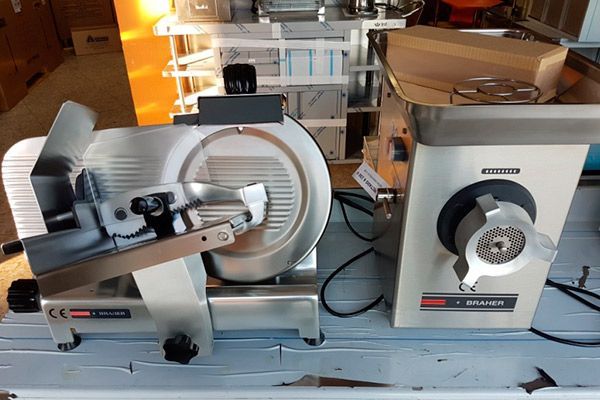 Una cortadora de carne y una picadora de carne una al lado de la otra sobre una superficie de acero inoxidable.