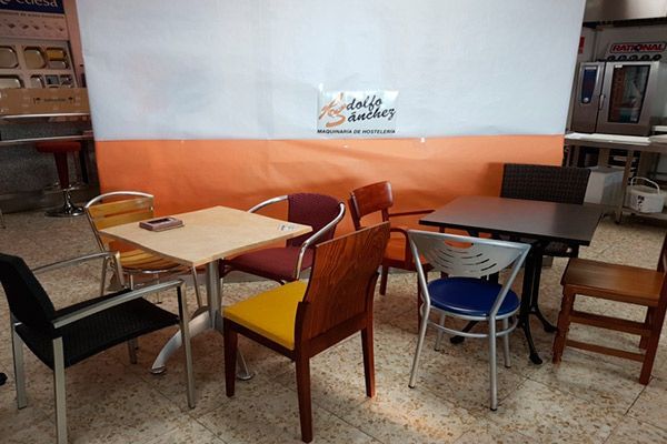 Zona de estar del restaurante con varias mesas y sillas. Pared blanca con franja naranja.