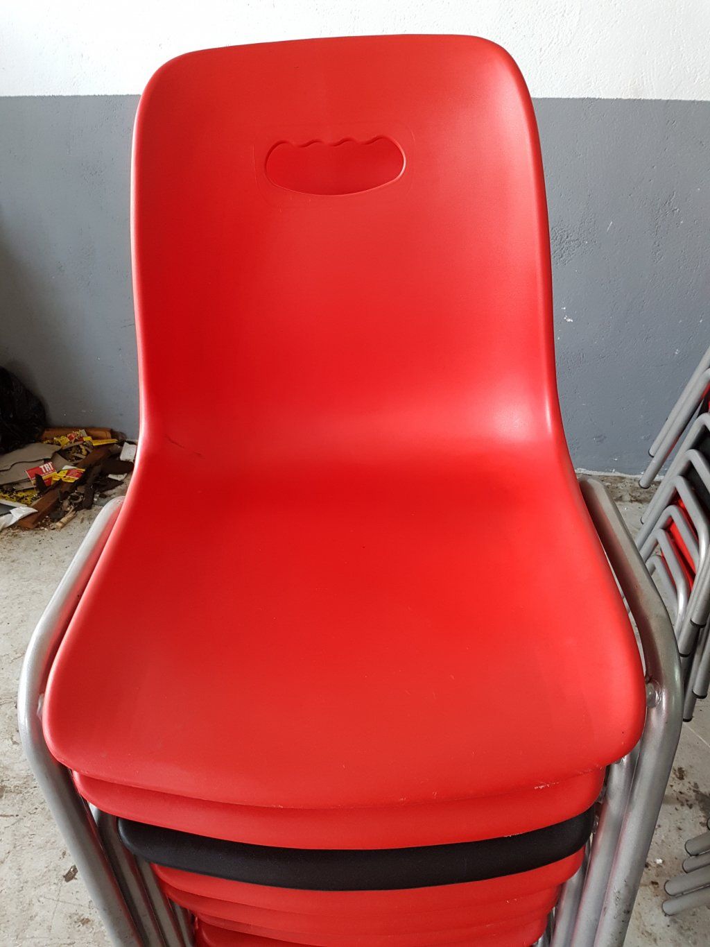 Sillas apiladas de plástico rojo con patas cromadas.