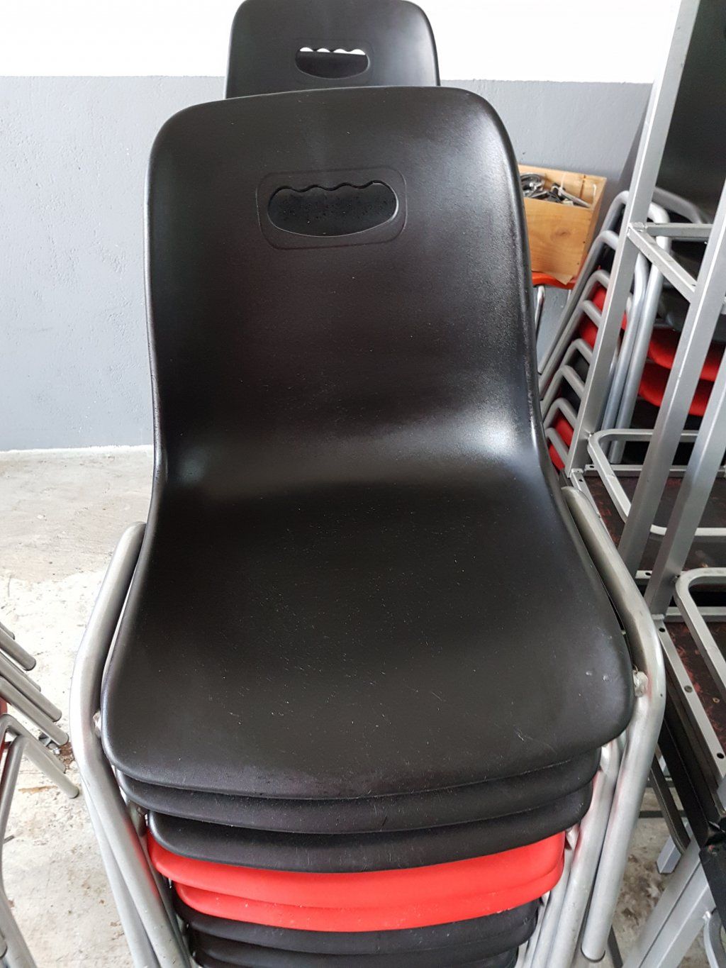 Sillas de plástico negro apiladas, silla roja visible entre ellas, marcos de metal.