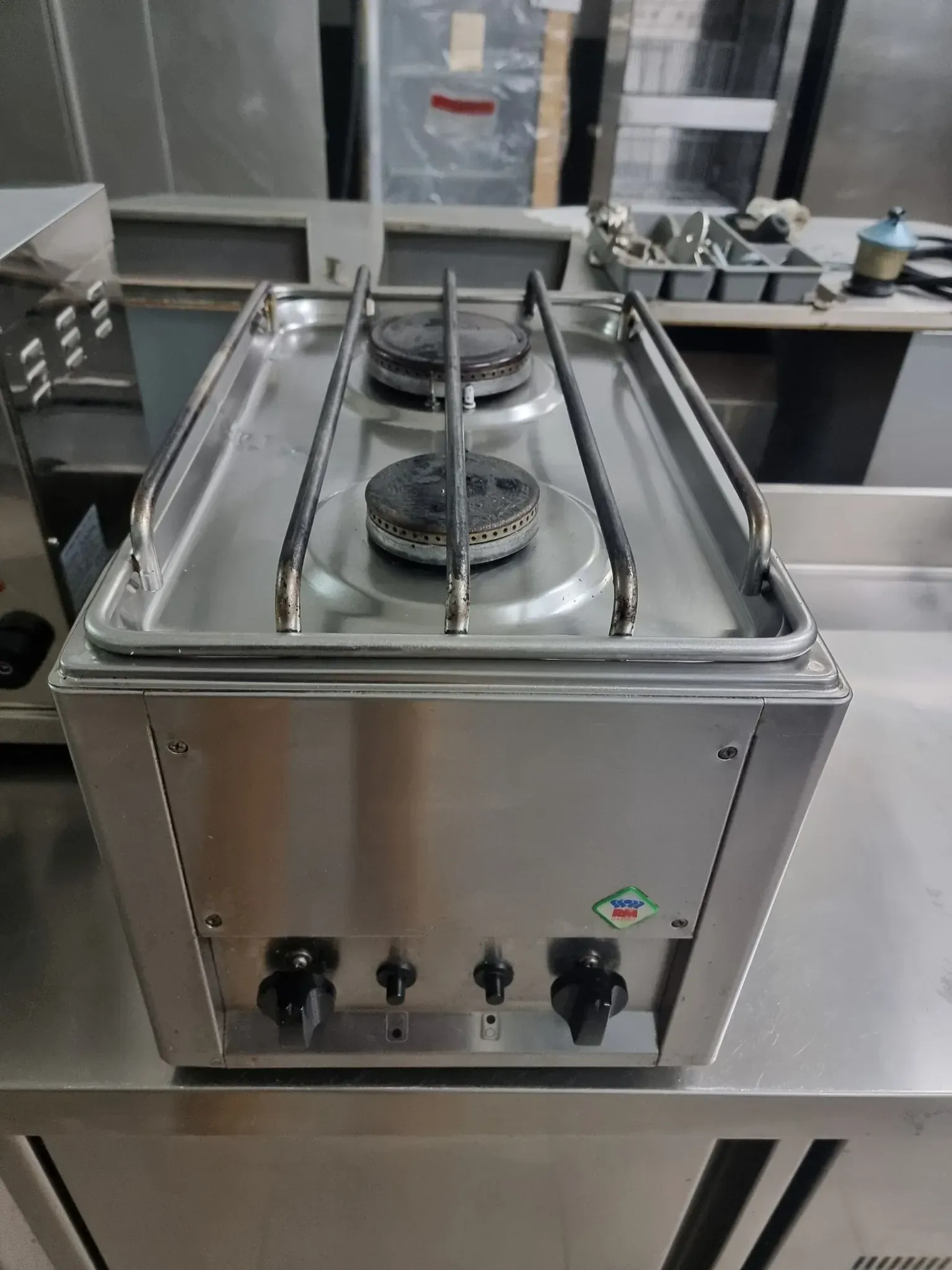 Estufa a gas de dos quemadores de acero inoxidable sobre una encimera de metal en una cocina comercial.