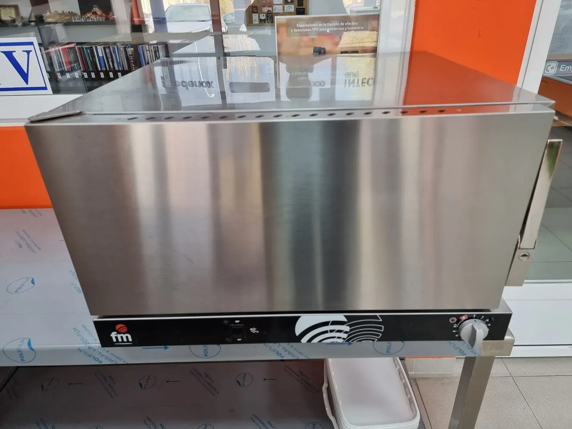 Calentador de alimentos de acero inoxidable sobre mesa de metal, con perilla de control de temperatura.