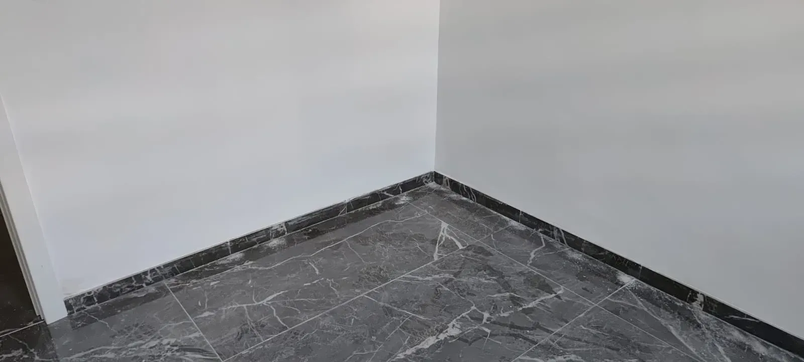 Esquina vacía de una habitación con paredes blancas y suelo oscuro con efecto mármol