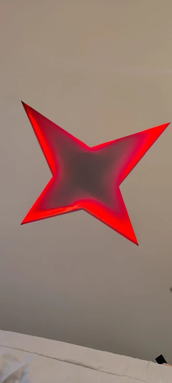 Luz de pared roja en forma de estrella, brillando sobre una pared beige.
