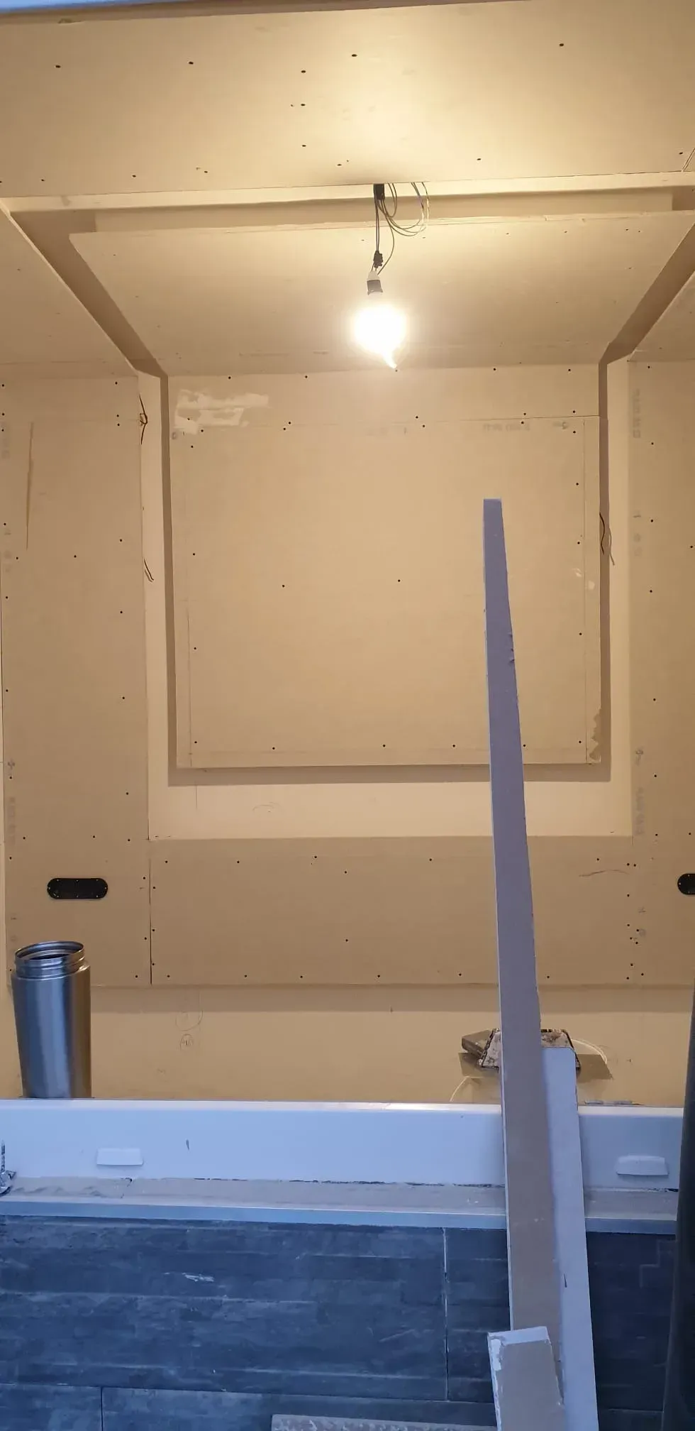 Baño a medio terminar, con paneles de yeso a la vista, una lámpara y un mueble de lavabo en primer plano