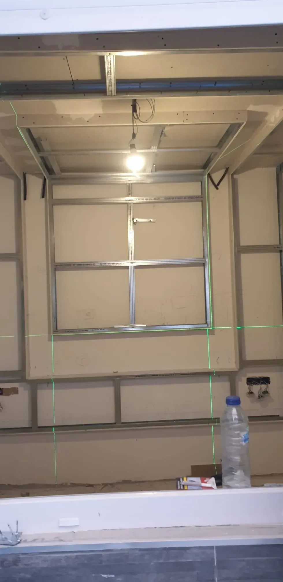 Habitación vacía con una ventana, una lámpara de techo y una mesa con una botella de agua en primer plano