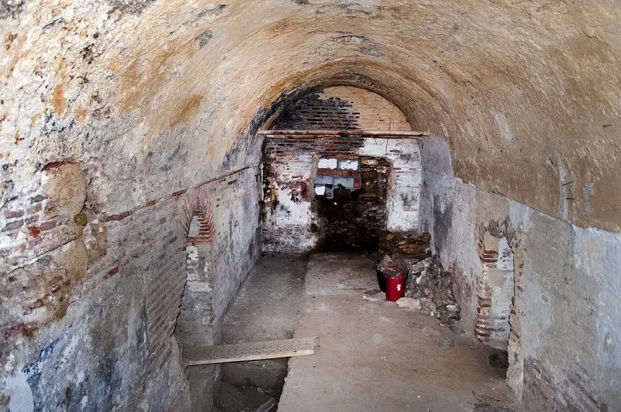 Túnel de piedra con techo abovedado, paredes irregulares y un pequeño cubo rojo en el suelo.