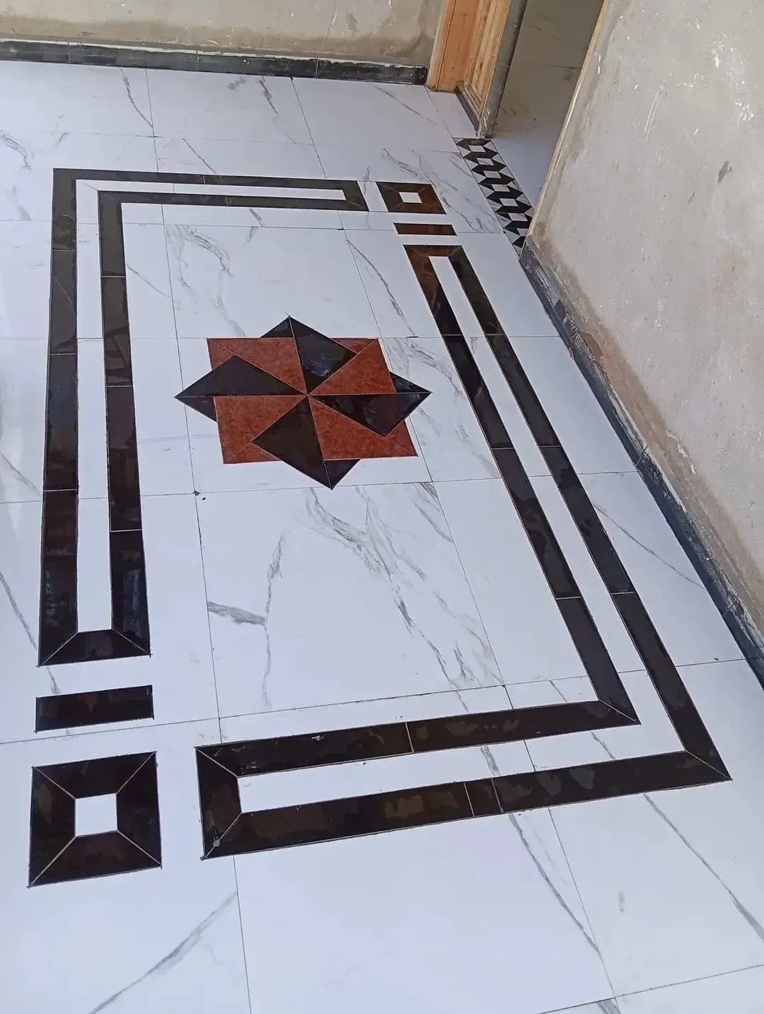 Suelo decorativo de baldosas con un borde negro y una estrella roja en el centro, junto a una pared