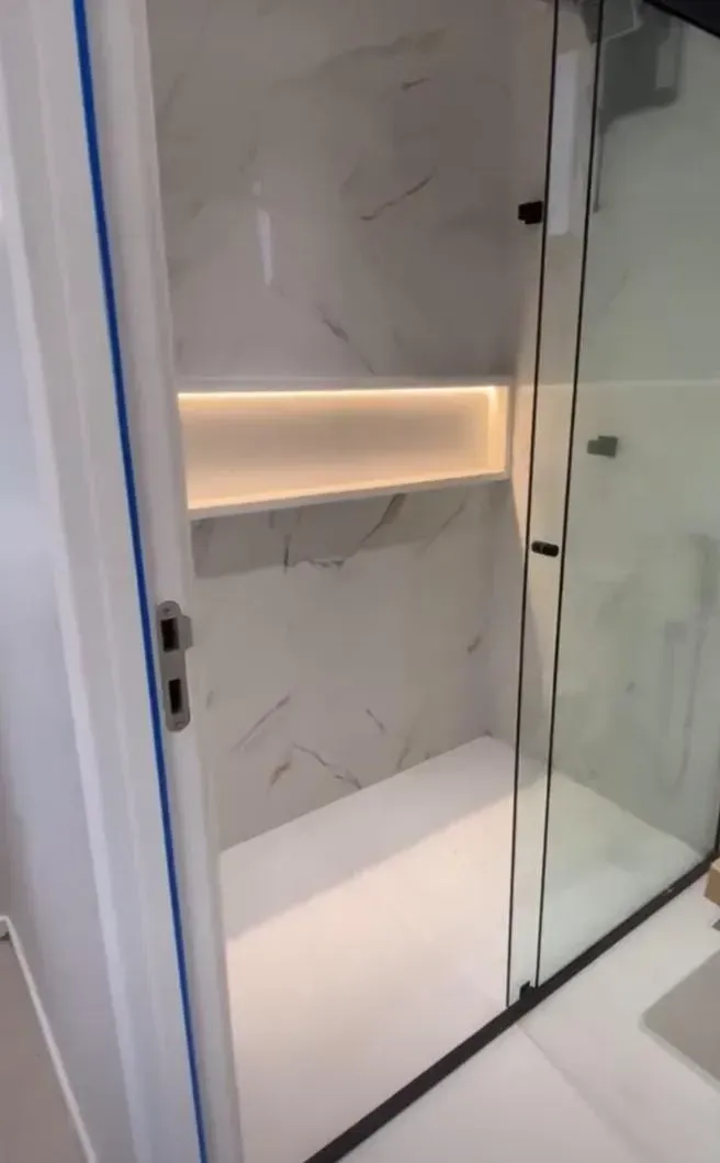 Ducha moderna con puerta de cristal, paredes efecto mármol y nicho empotrado iluminado