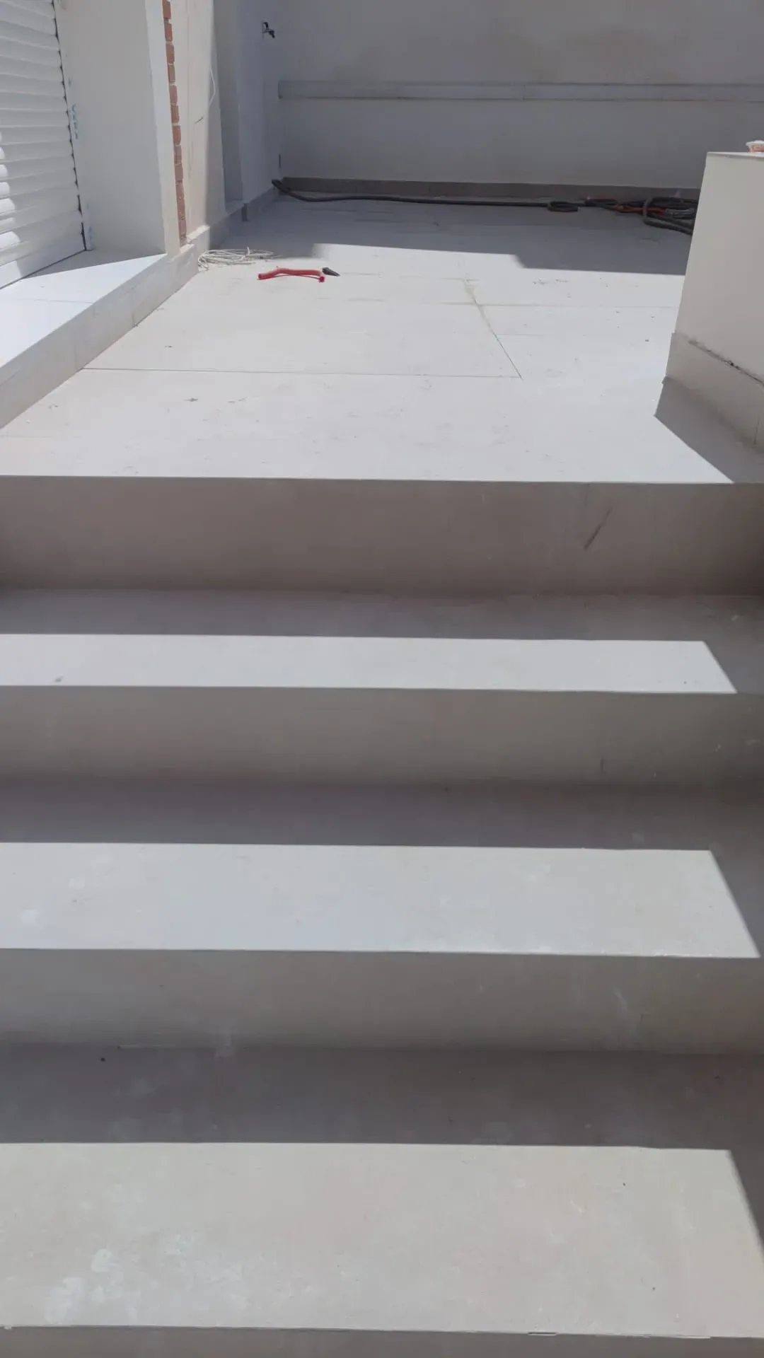 Escalones exteriores de hormigón blanco que conducen a un rellano soleado con un pequeño objeto rojo al fondo