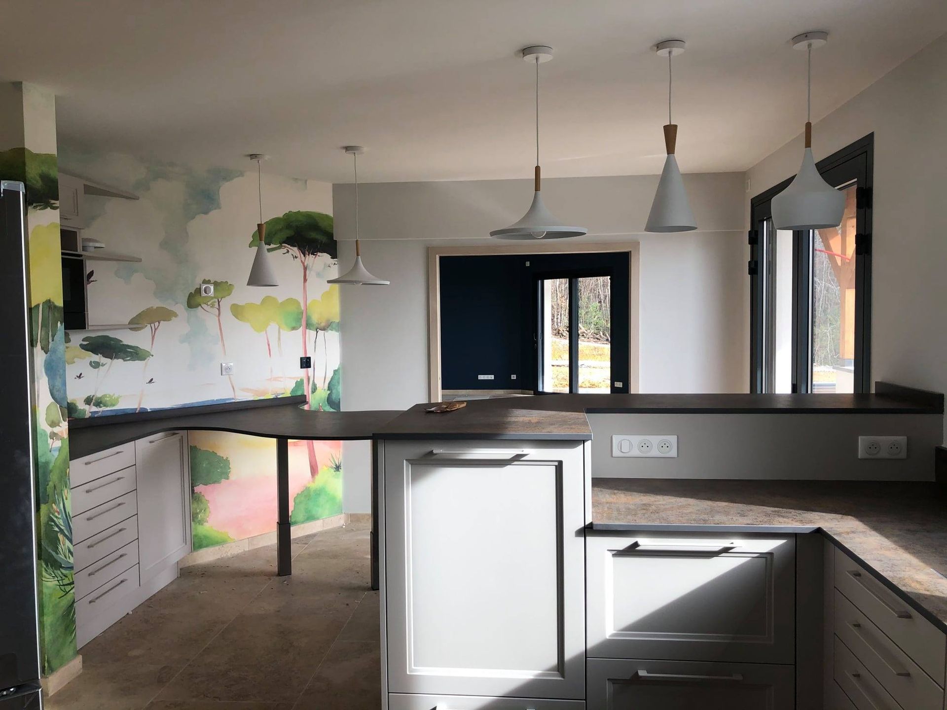 Cuisine moderne avec armoires blanches, îlot central et suspensions lumineuses. Fresque murale.