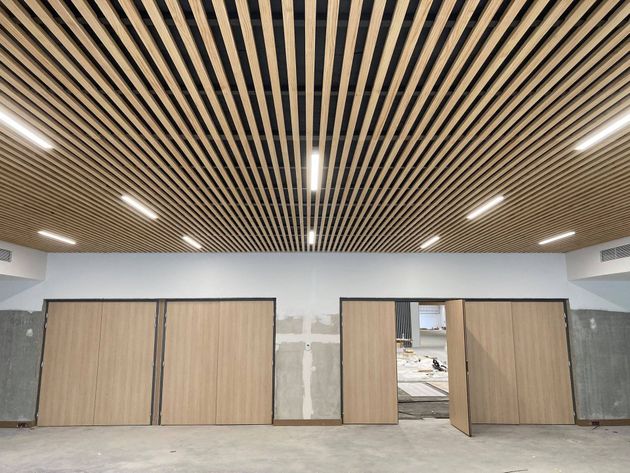Plafond à lattes de bois avec spots encastrés, au-dessus de portes en bois clair et de murs bruts.