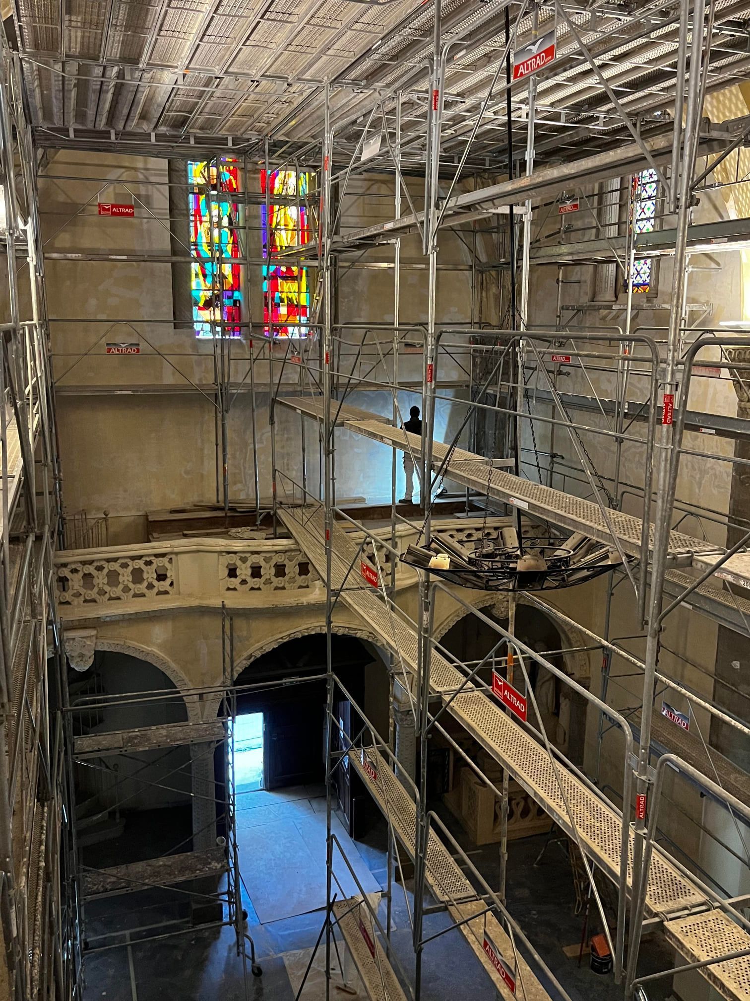 Intérieur d'un bâtiment avec échafaudages et vitrail. Porte visible au fond du couloir.