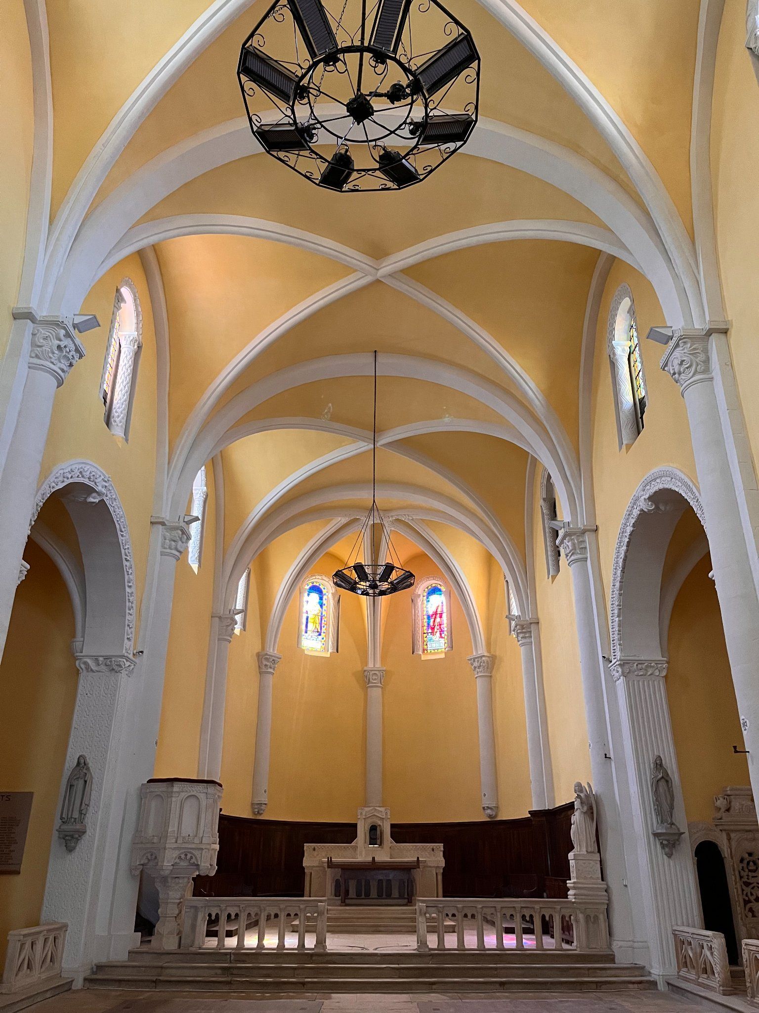 Intérieur d'une église avec plafond voûté, vitraux et ornements. Murs jaunes, boiseries blanches.