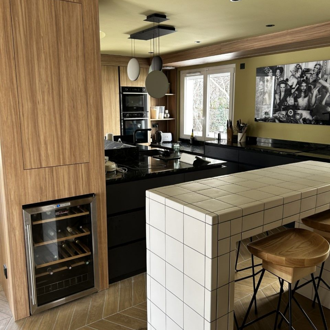 Cuisine avec placards en bois, comptoirs noirs, îlot central carrelé de blanc et cave à vin.