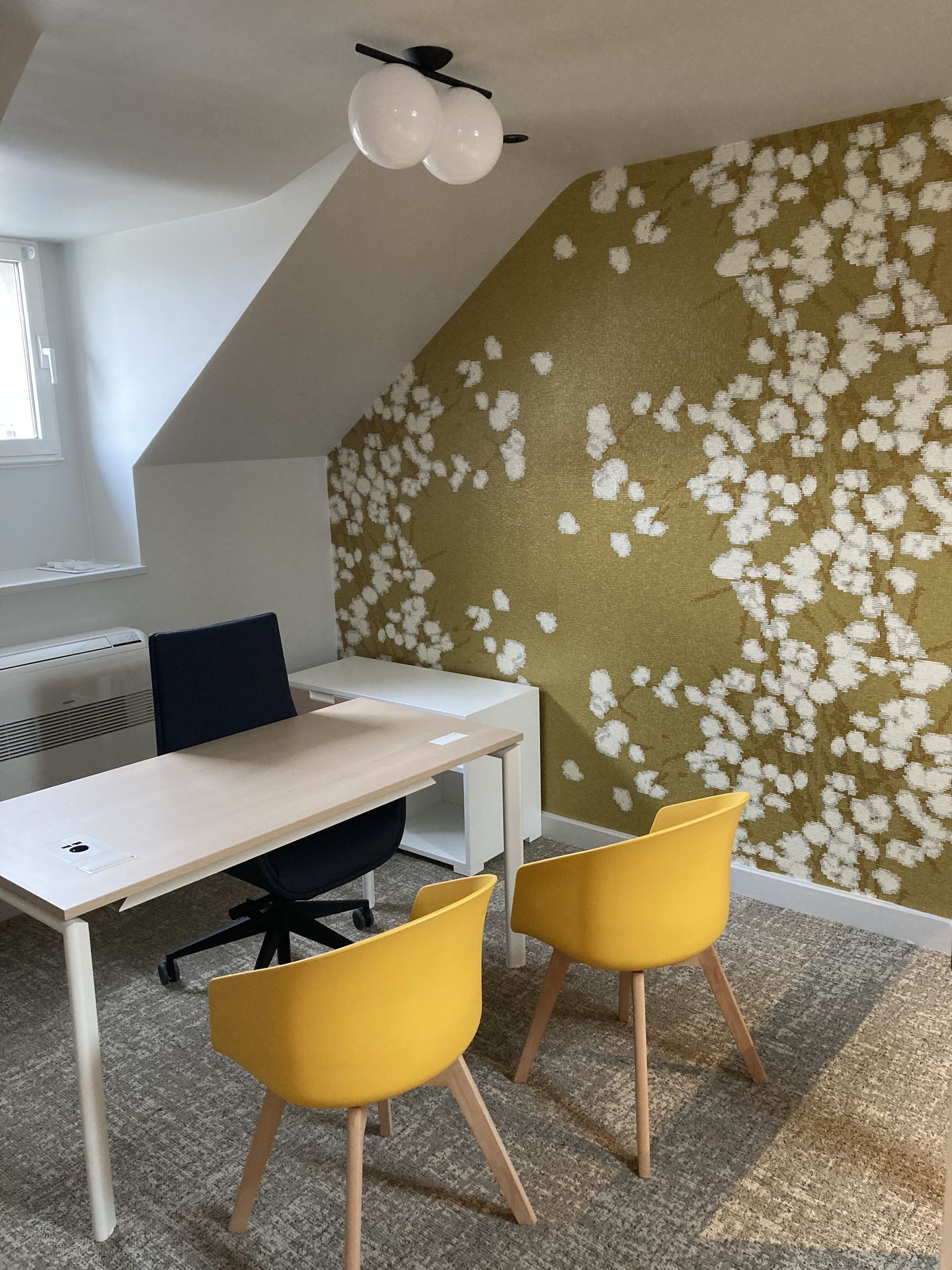 Espace de bureau avec bureau, chaises jaunes et mur à motifs floraux.
