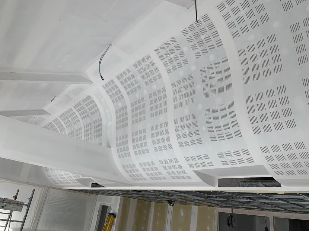 Panneaux de plafond blancs perforés dans un contexte de construction, partiellement installés.