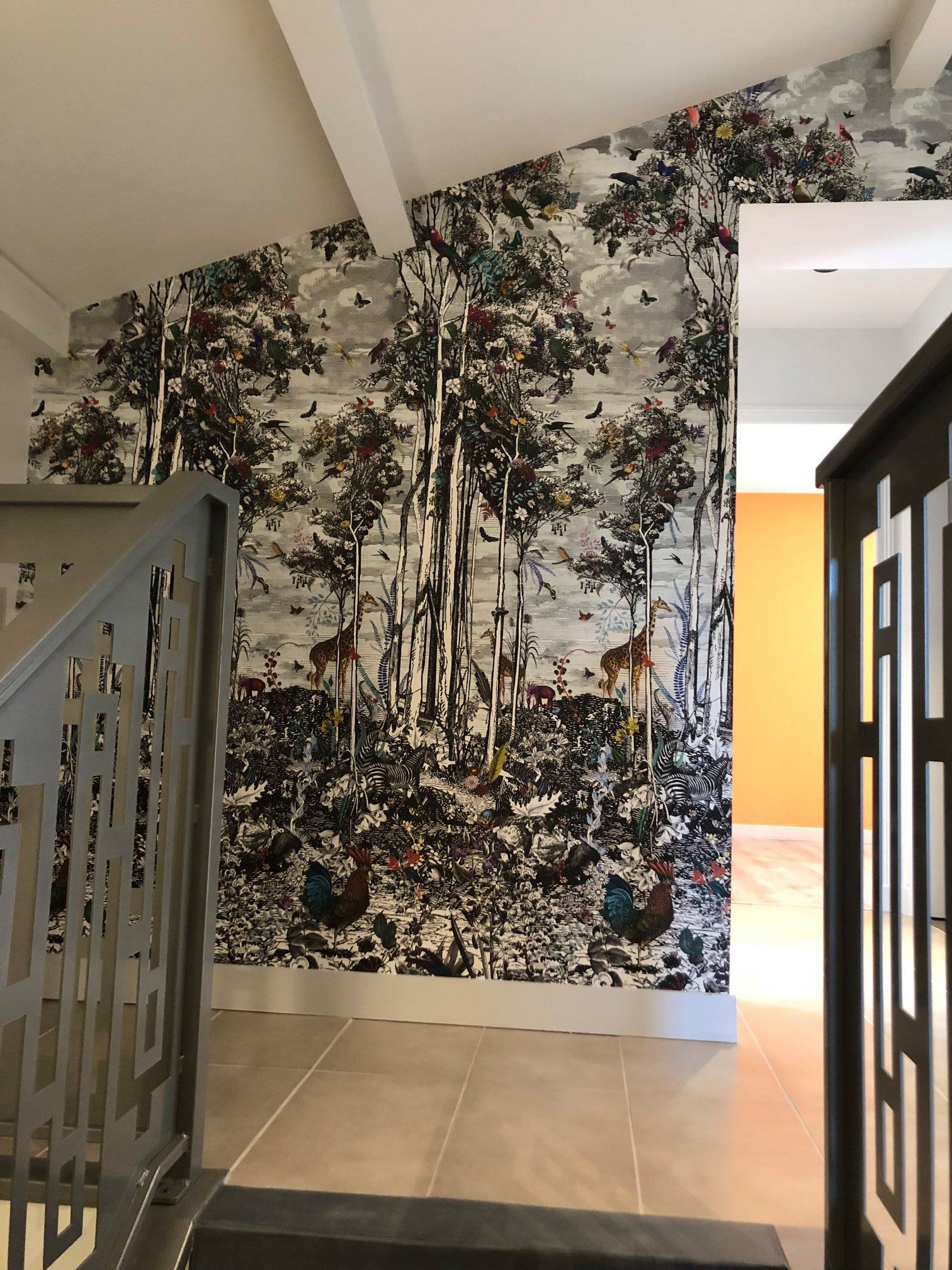 Le mur d'une maison est tapissé d'un papier peint à motif de forêt. De part et d'autre, on aperçoit un escalier et un encadrement de porte.