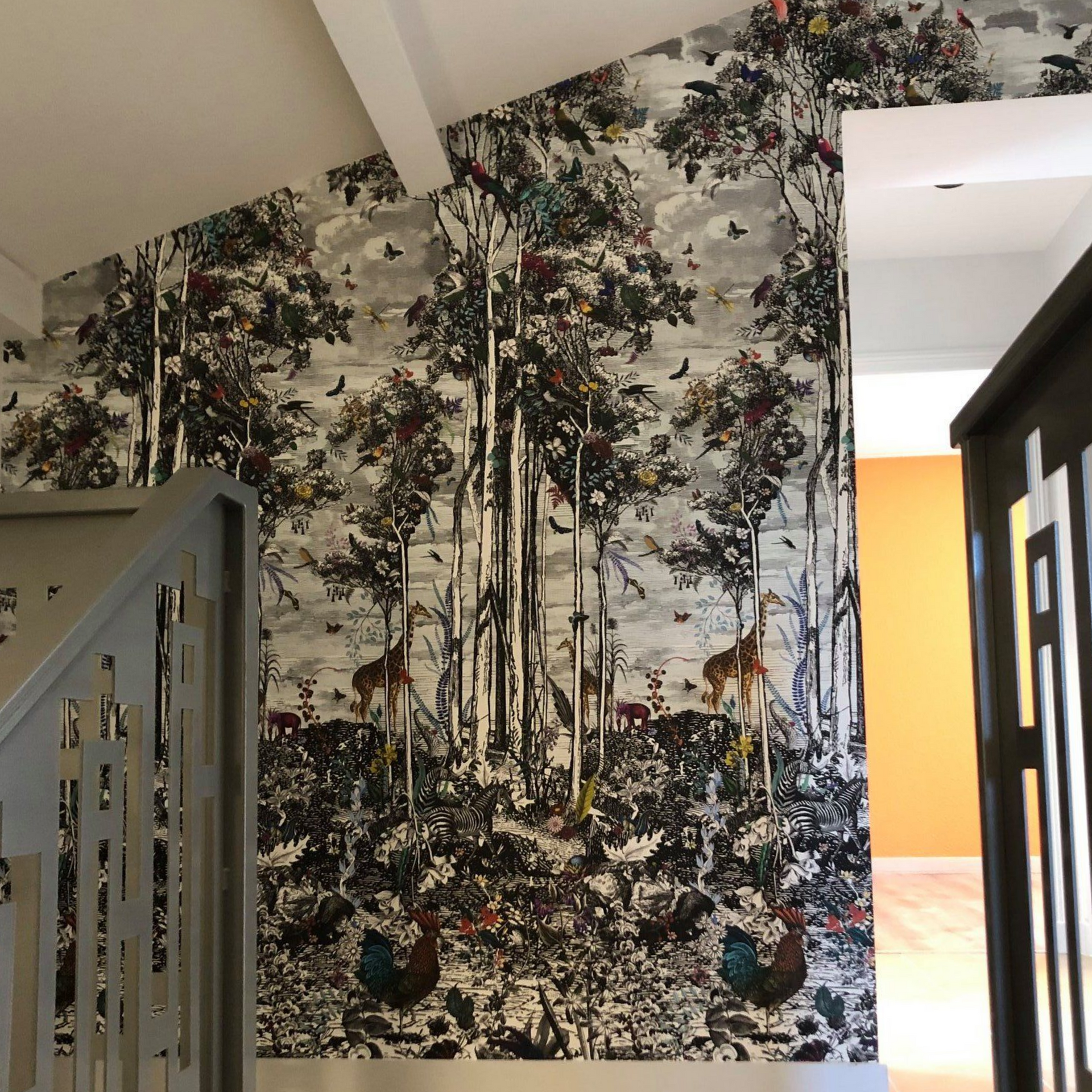 Couloir avec papier peint à motifs représentant une scène de forêt avec des animaux ; escalier avec rampe grise.