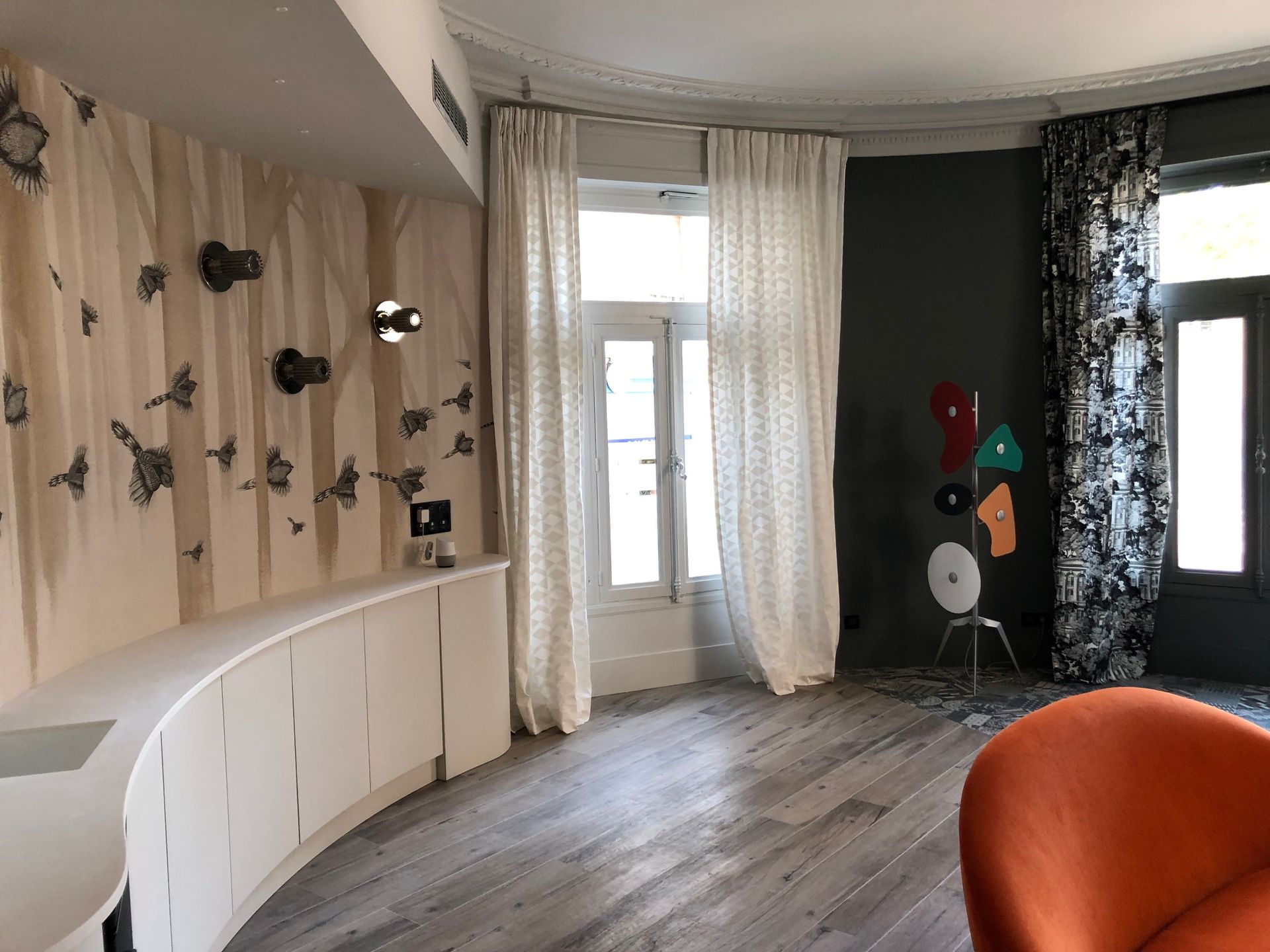 Intérieur élégant avec placards blancs aux formes arrondies, rideaux et œuvres d'art. Chaise orange visible.