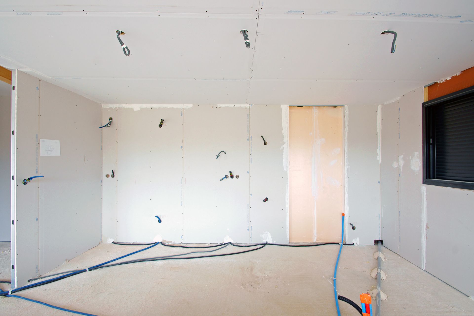 Pièce intérieure en construction, avec des murs en plaques de plâtre, des câbles apparents et une porte.