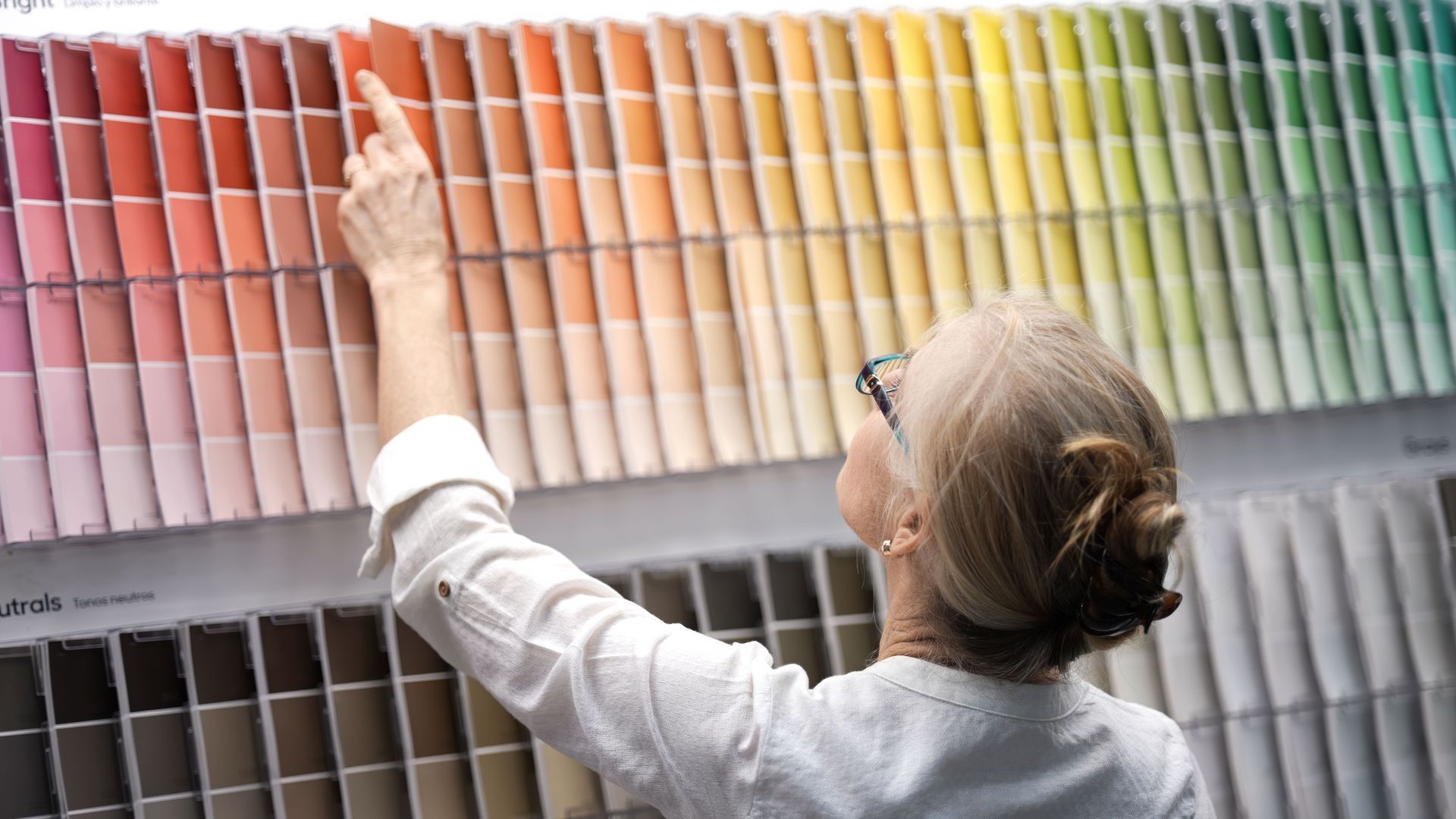 Une personne examine des échantillons de peinture, en désignant une teinte rouge orangée, dans un magasin de bricolage.