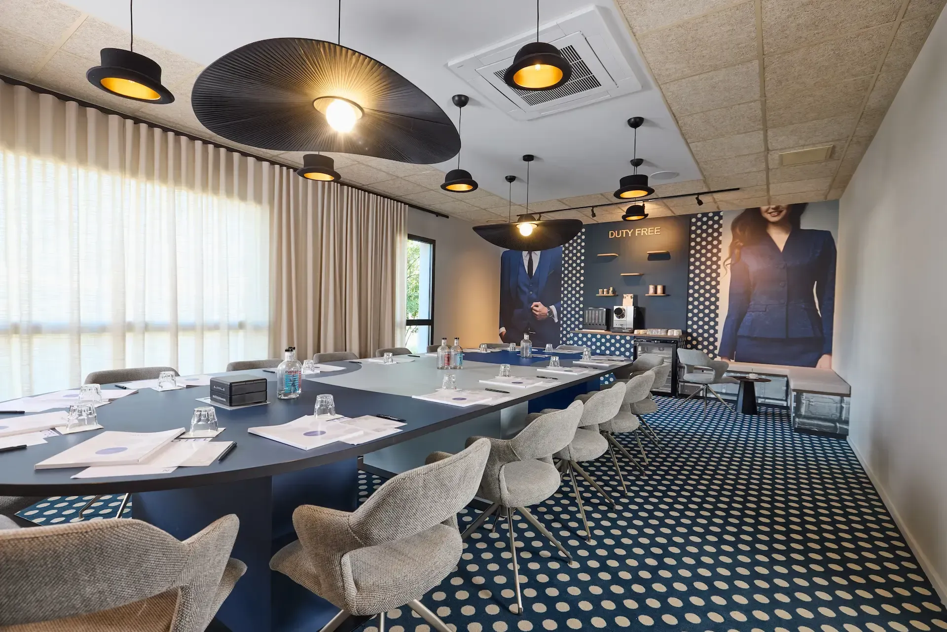 Salle de conférence avec table ovale bleue, moquette à motifs, éclairage décoratif et grand portrait de femme.