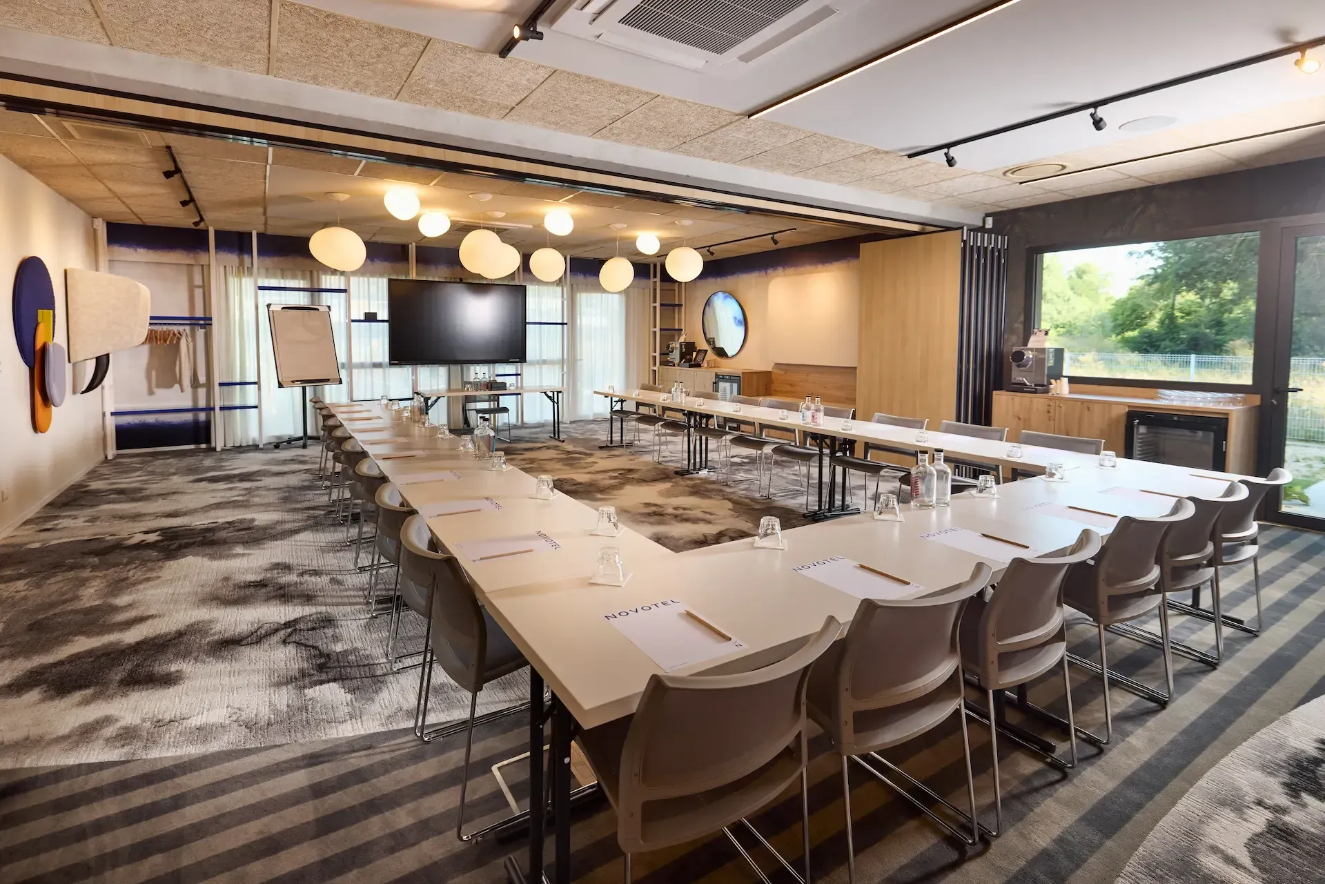 Salle de conférence avec table en forme de U, chaises et grand écran de télévision.