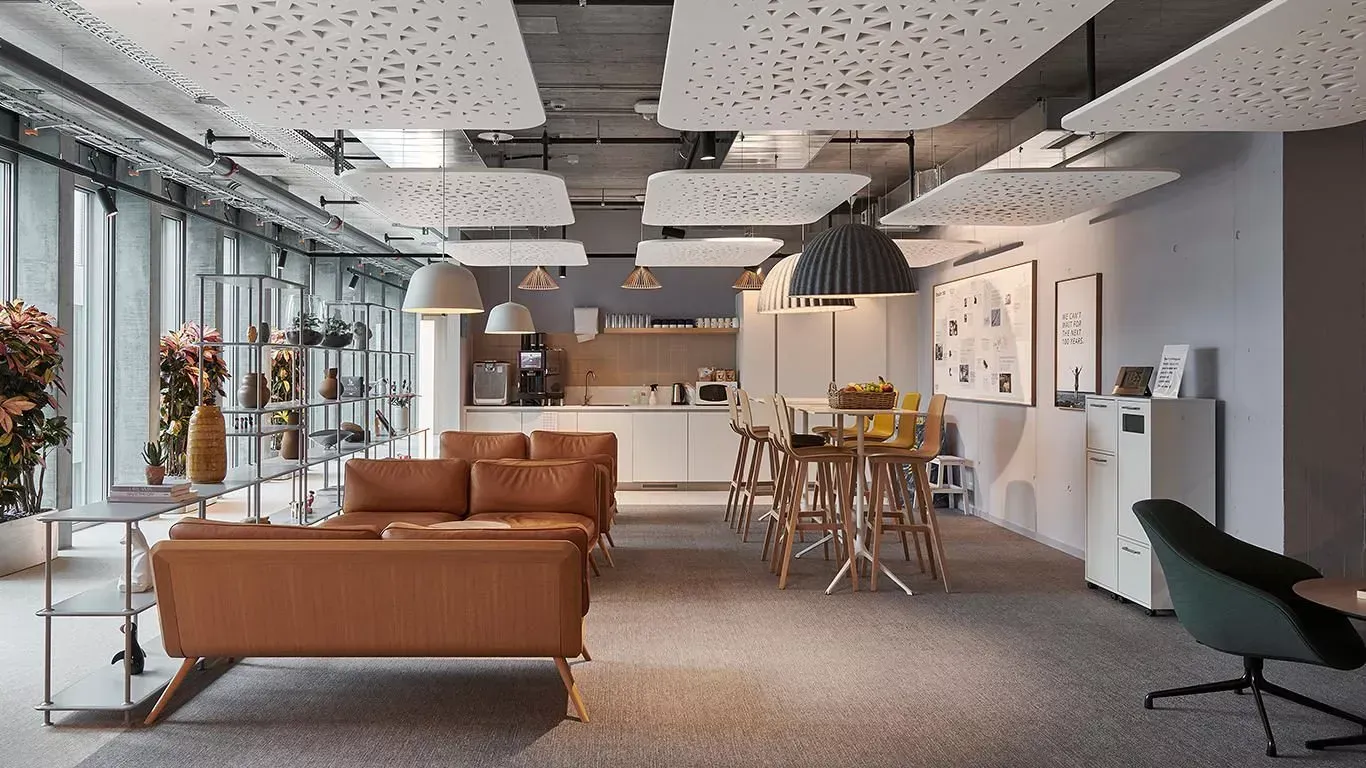 Intérieur de bureau moderne avec canapé marron, cuisine, coin repas et panneaux de plafond insonorisés.