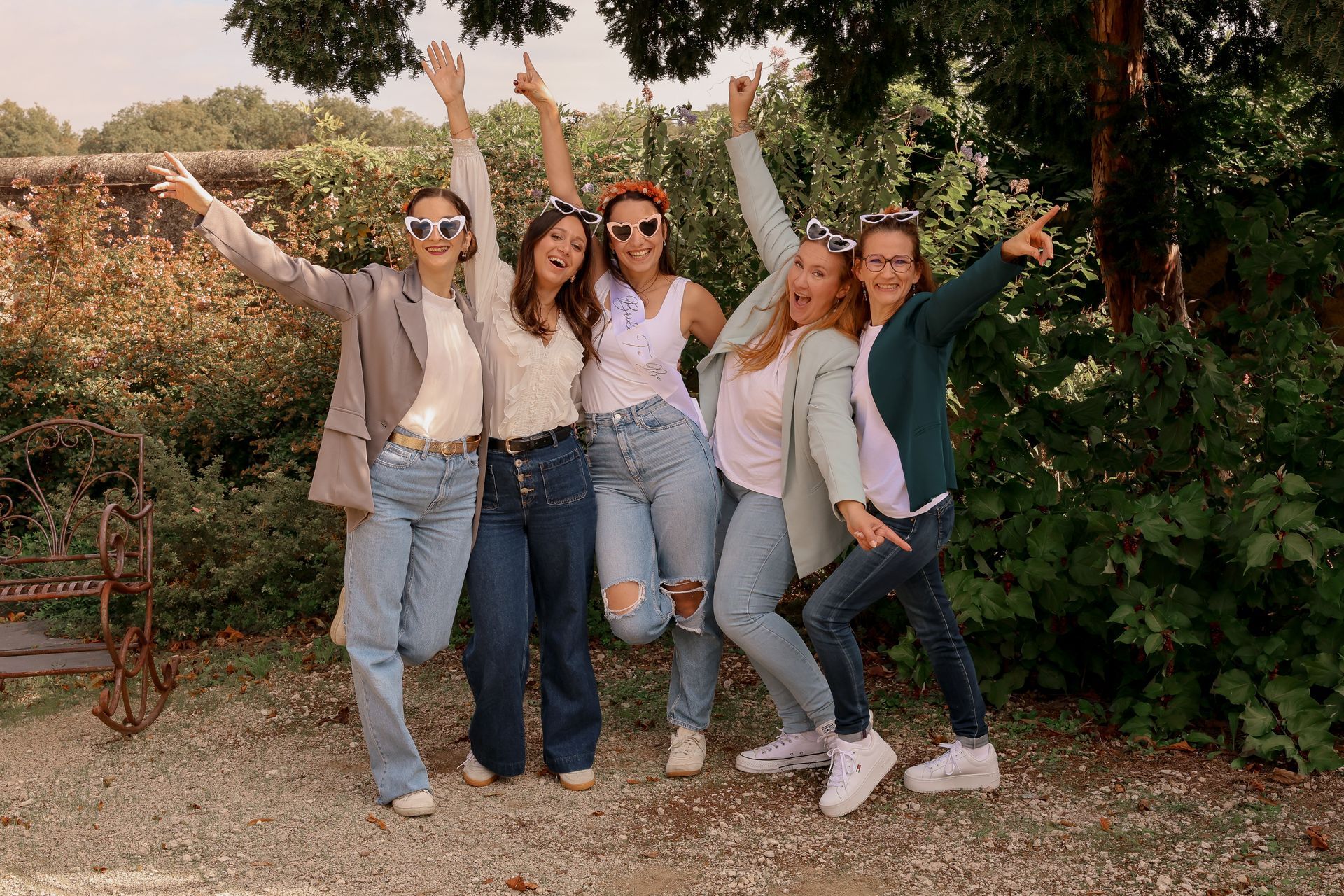Cinq personnes, les bras levés, souriant à l'extérieur en tenue décontractée.