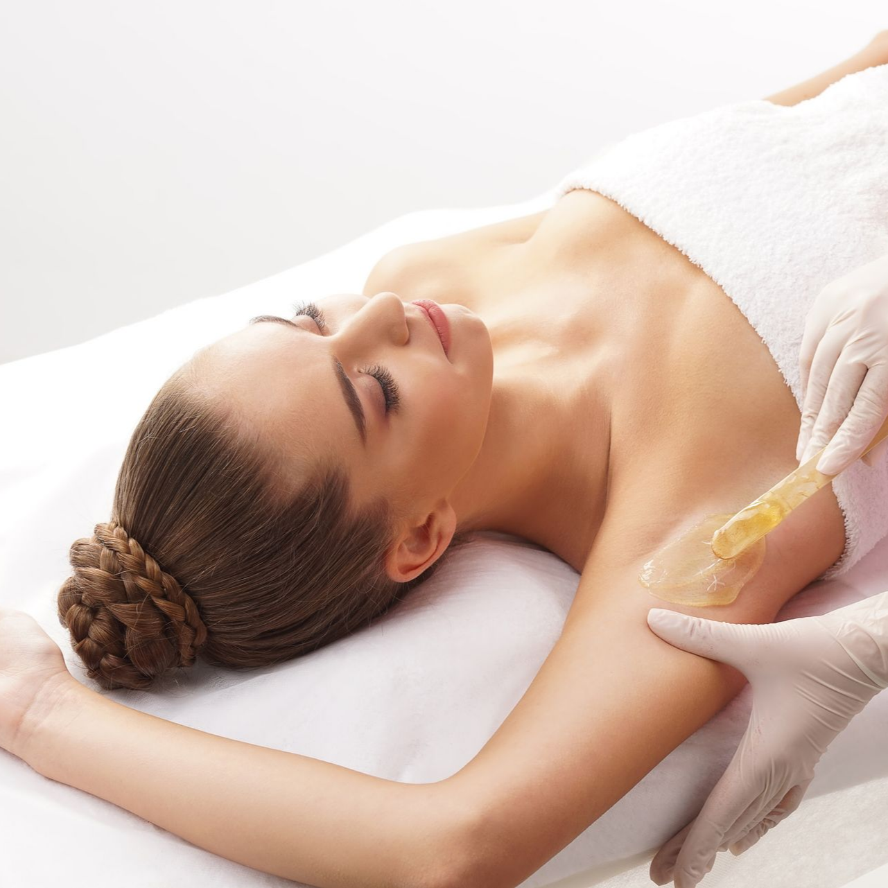 Une femme se fait épiler les aisselles à la cire dans un spa. Un praticien applique la cire sur son bras à l'aide d'une spatule.