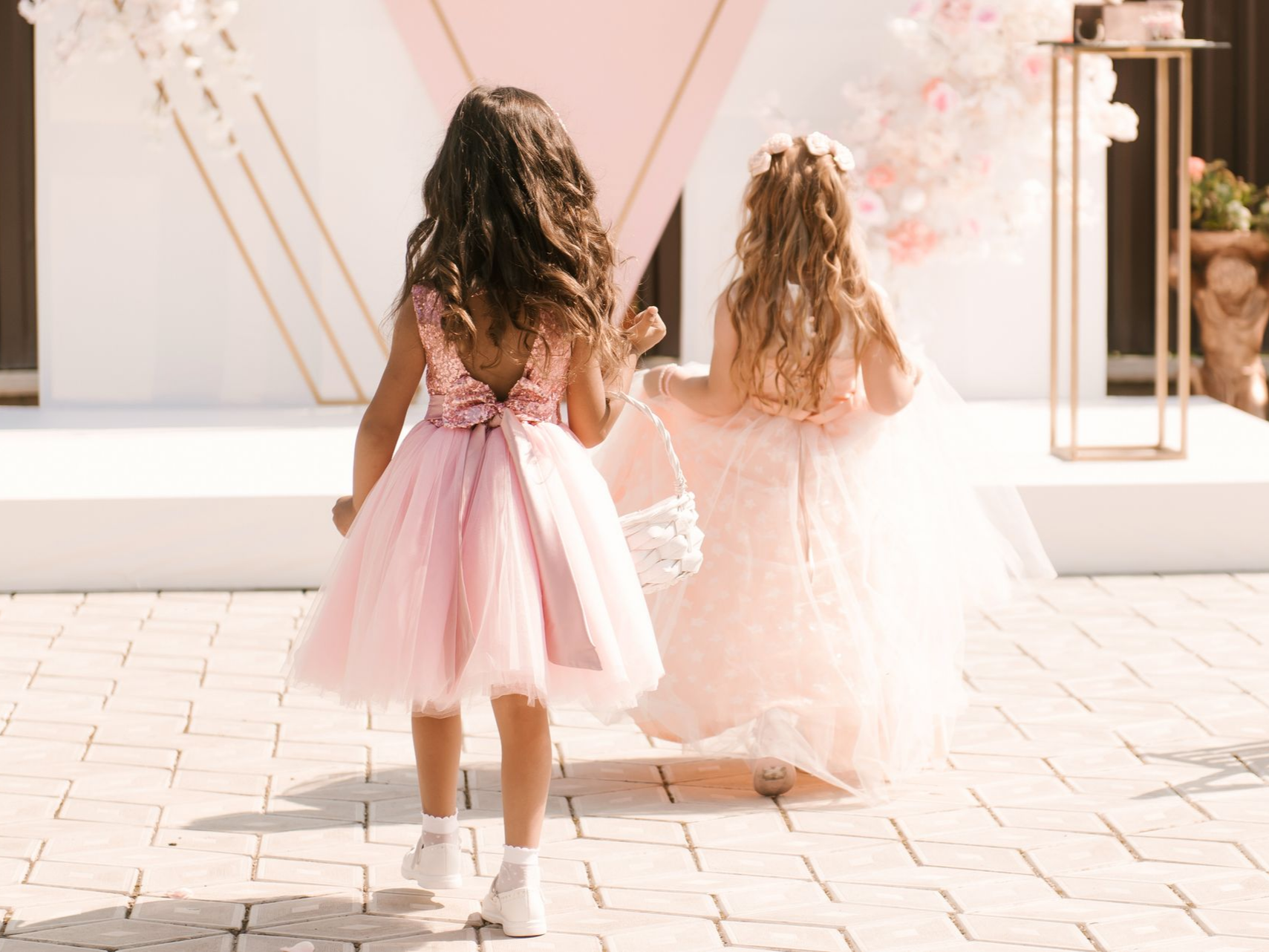 Deux jeunes filles en robes roses marchent à l'extérieur, l'une portant un panier.