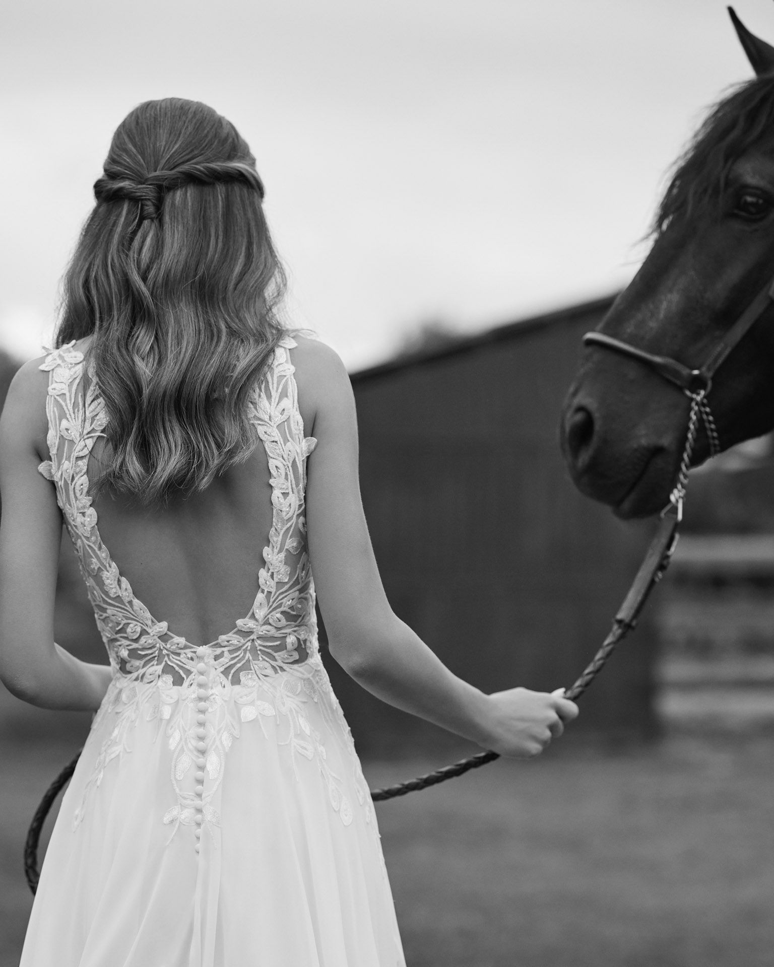 Mariée dans une robe de mariée en dentelle, vue de dos, boutonnée par une demoiselle d'honneur.