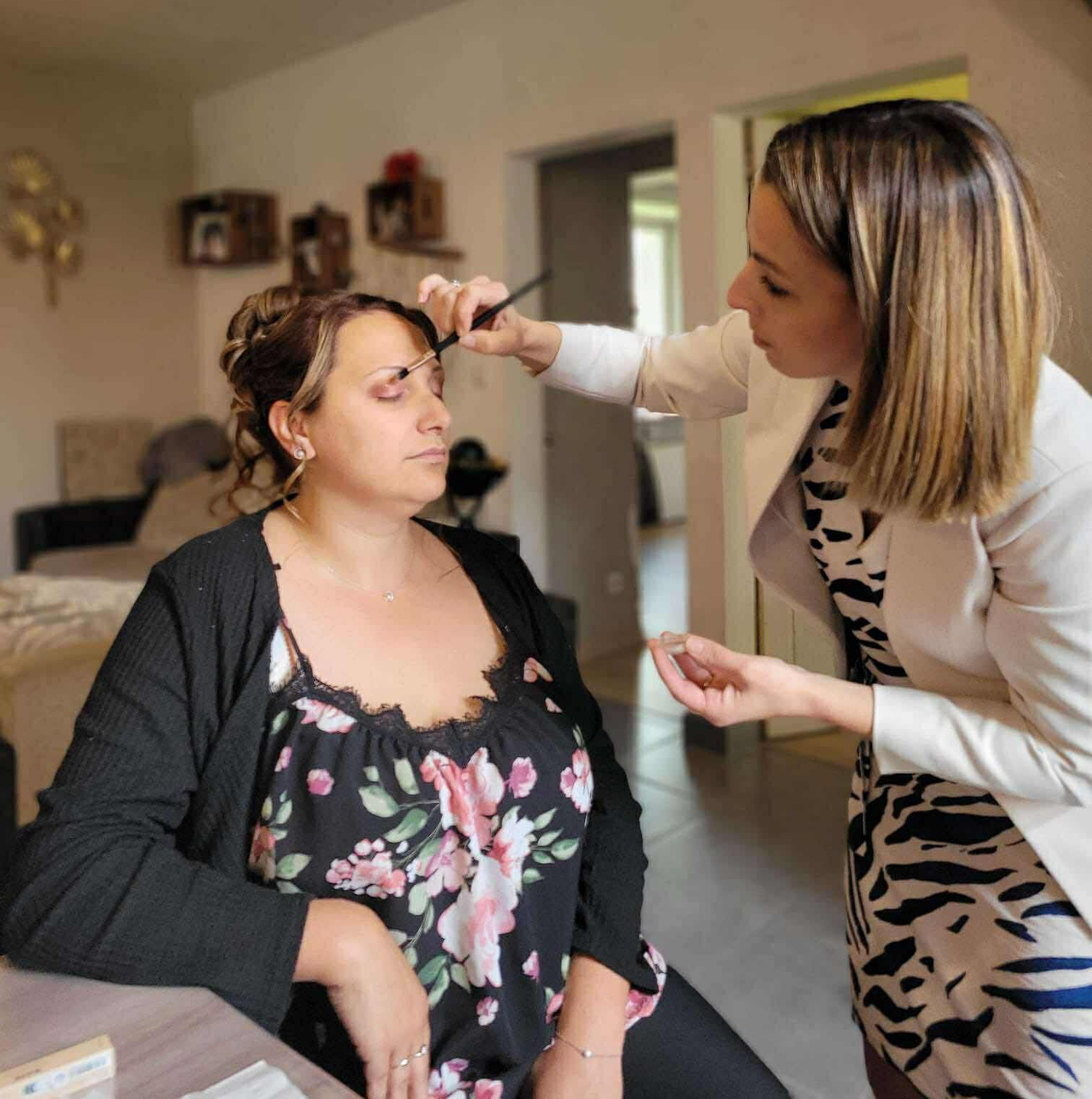 La mariée en robe blanche ornée de perles regarde par-dessus son épaule. Le marié en costume sourit derrière elle. Décor extérieur.