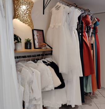 Intérieur de boutique de mariage avec robes de mariée, coin salon, grand miroir et sol carrelé.