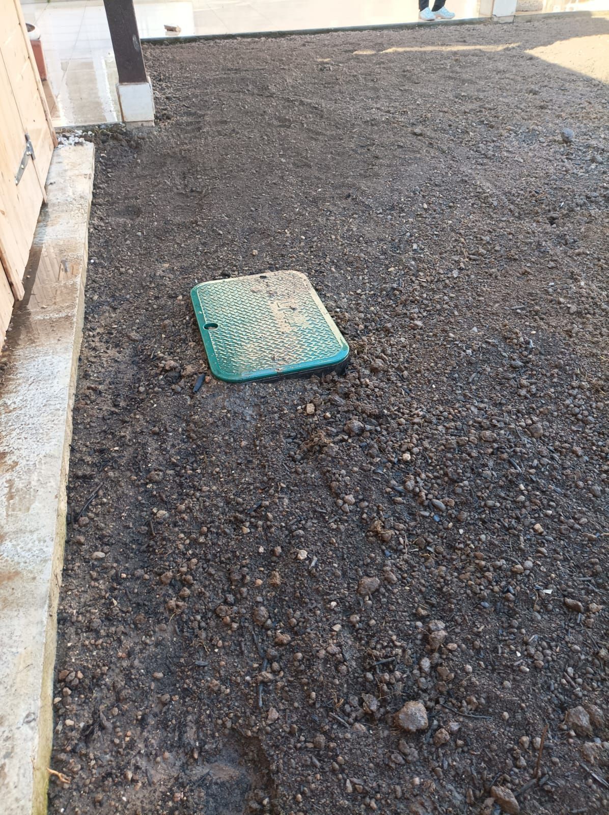 Un couvercle de regard vert est posé sur un tas de terre.