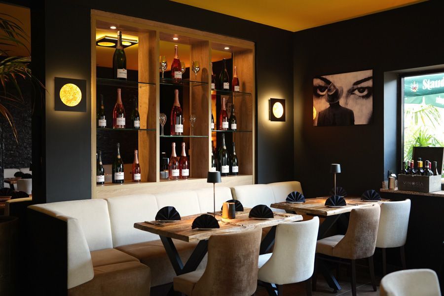 Moderner Restaurant-Essbereich mit weißen Stühlen, Holztischen, dunklen Wänden und Wandkunst