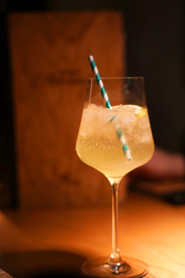 Ein hochstieliger Cocktail mit Eis und einem gestreiften Strohhalm auf einem warm beleuchteten Tisch