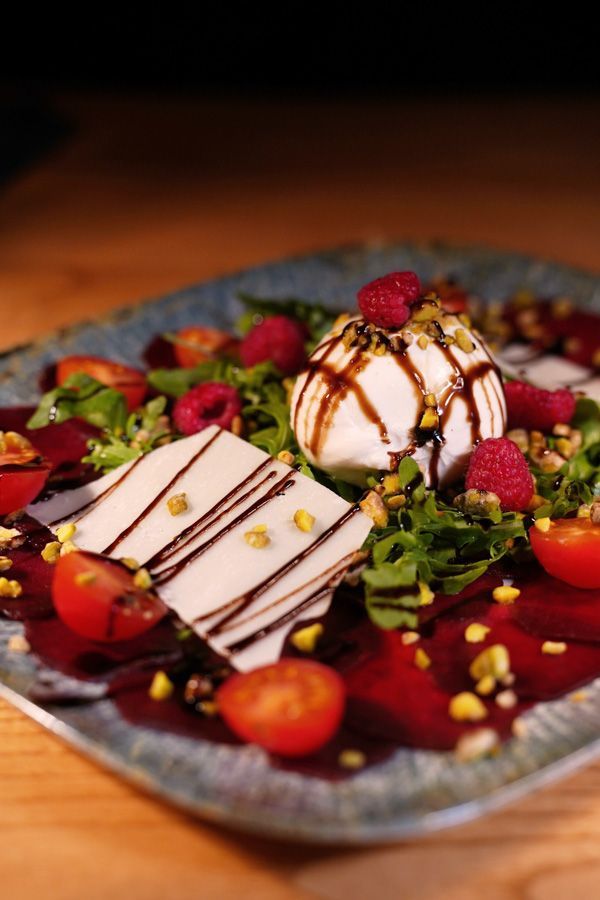 Dessertteller mit Käsekuchenstücken, Beeren und Schokoladensauce auf einer dunklen Platte