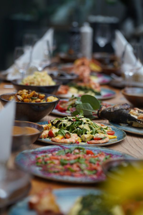 Lange Festtafel mit farbenfrohen Gerichten und Salaten, gedeckt für ein gemeinsames Essen im Innenbereich.