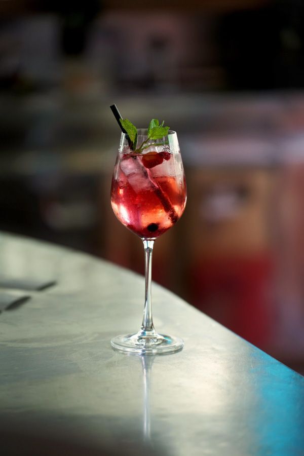 Roter Cocktail mit Minze in einem Stielglas auf einem Bartresen