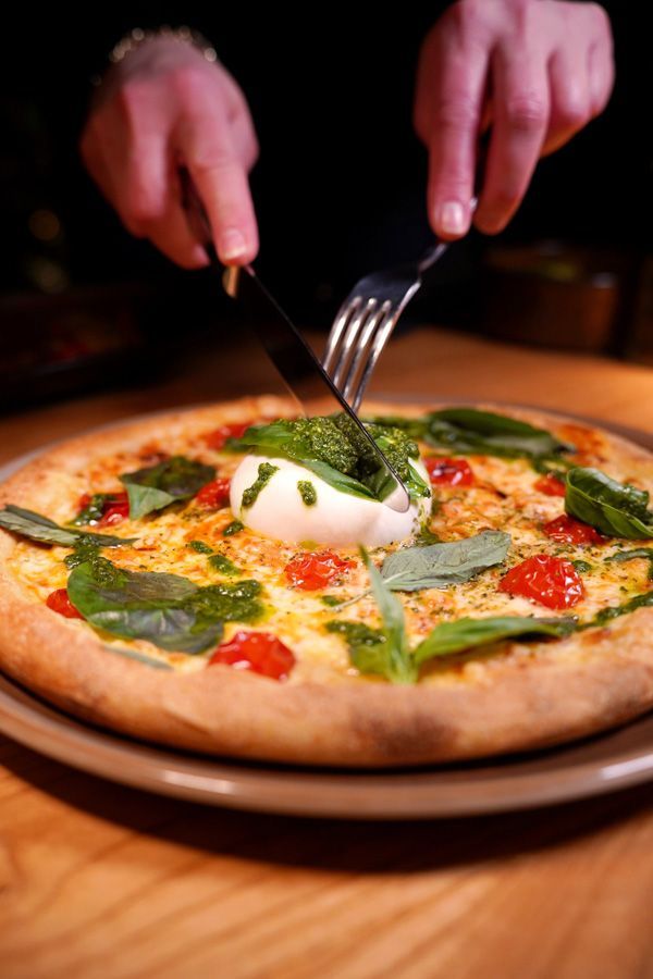 Hände schneiden auf einem Holztisch in eine Käse-Basilikum-Pizza.